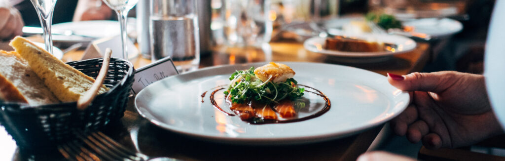 A person sitting over a gourmet meal at a long table with numerous plates and wine glasses.